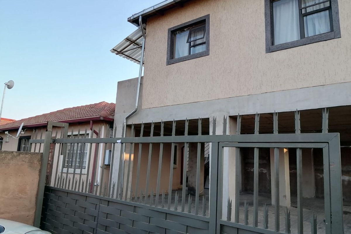 Front view of a two-story residential property featuring a metal security gate, concrete pillars, and textured exterior wall finishes.