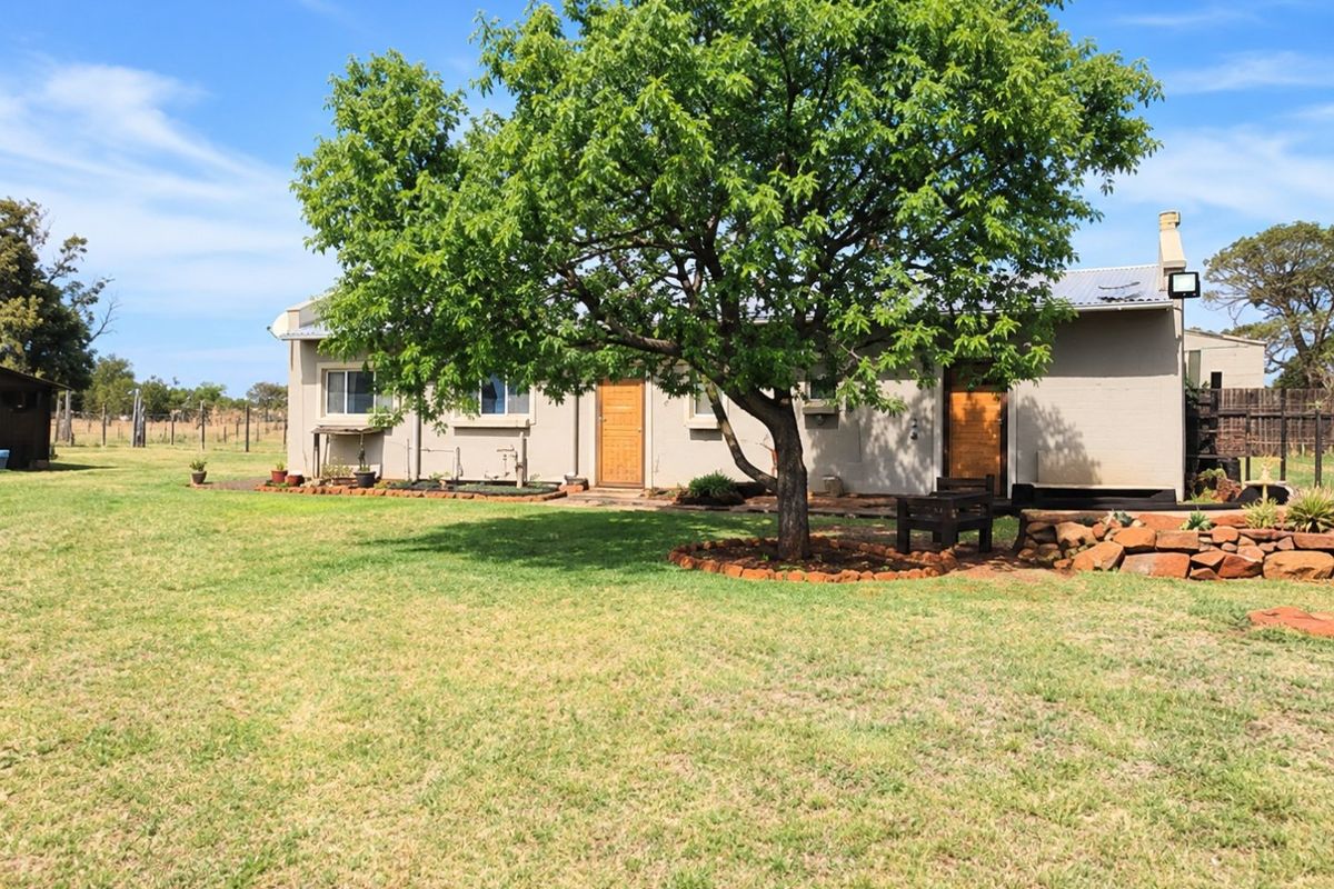 Rear view of the property featuring a large established tree, stone landscaping, and a well-maintained lawn area.