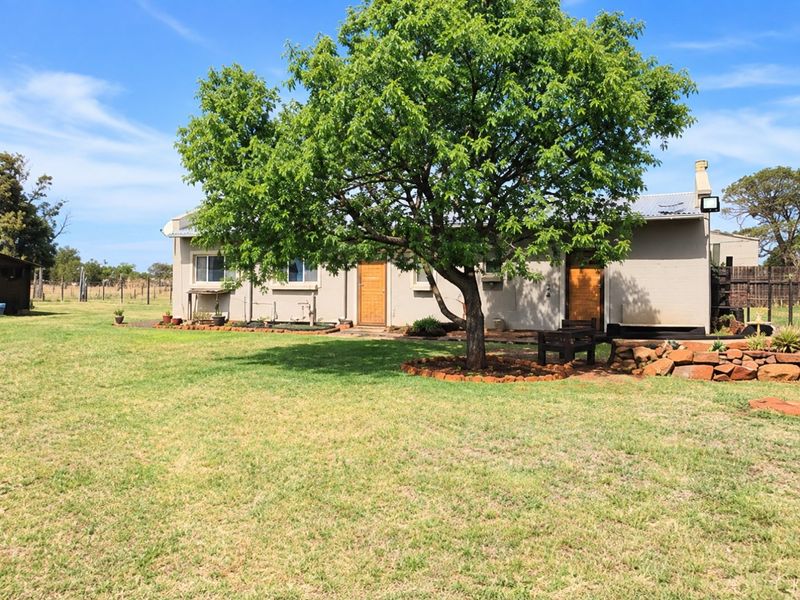 Rear view of the property featuring a large established tree, stone landscaping, and a well-maintained lawn area.