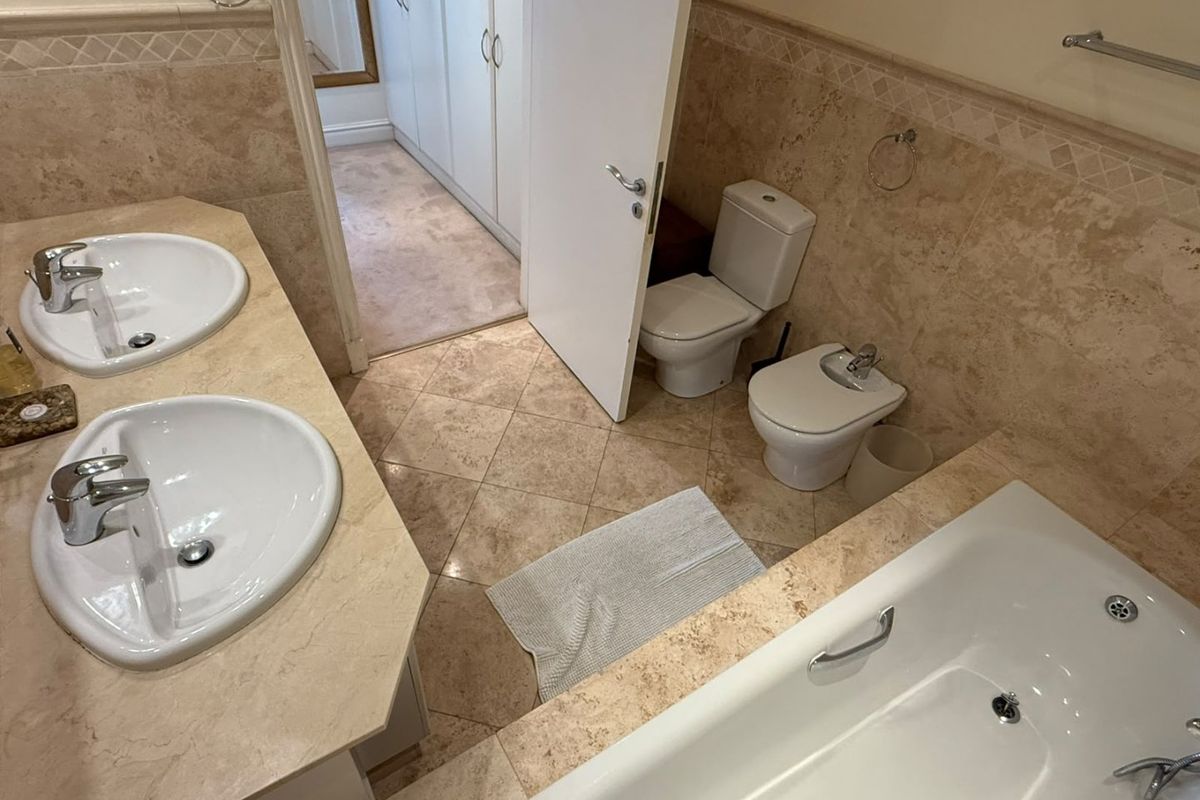 Spacious bathroom featuring a double vanity, built-in bathtub, toilet, and bidet, finished with neutral stone tiling and ample built-in storage.