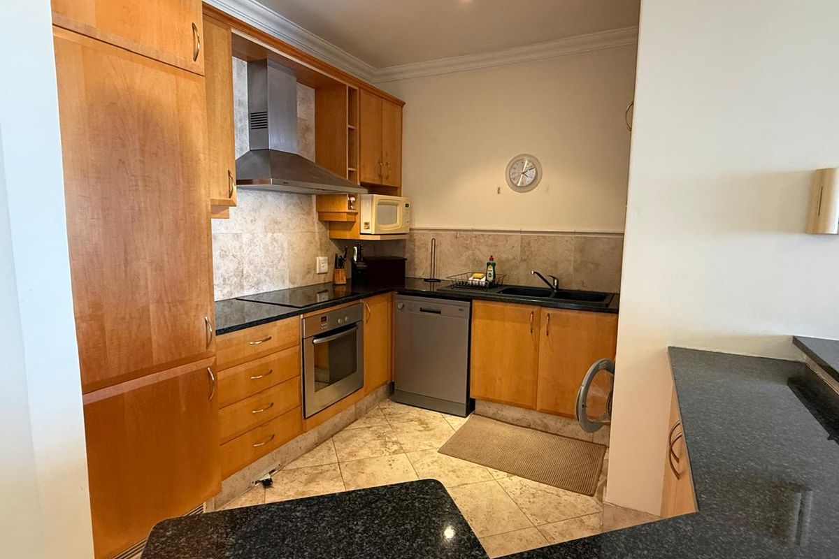A functional kitchen featuring warm-toned wooden cabinetry, granite countertops, a built-in oven with extractor fan, and tiled flooring throughout.