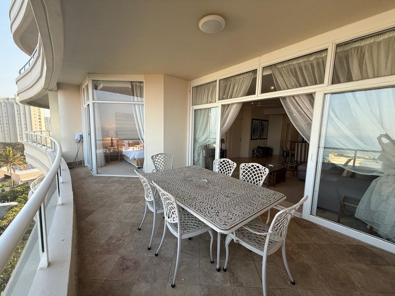 Spacious covered balcony featuring tiled flooring, a glass balustrade, and large sliding glass doors providing seamless access to the interior living areas.