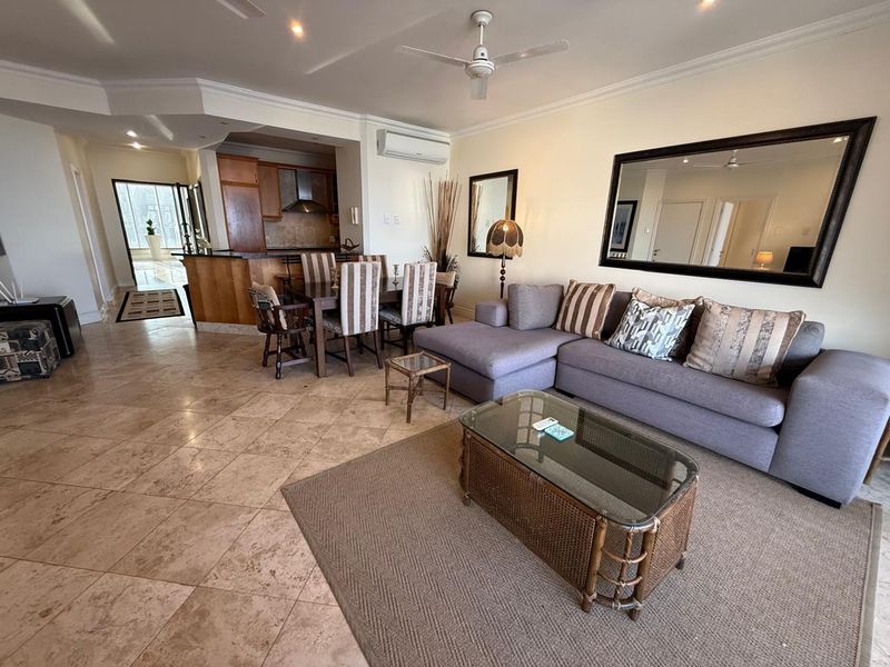 Open plan living and dining area featuring stone floor tiles, a ceiling fan, and an integrated kitchen with a breakfast bar.