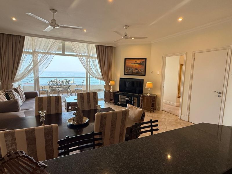Spacious open-plan living and dining area featuring tiled floors, ceiling fans, and large sliding doors opening onto a balcony with ocean views.