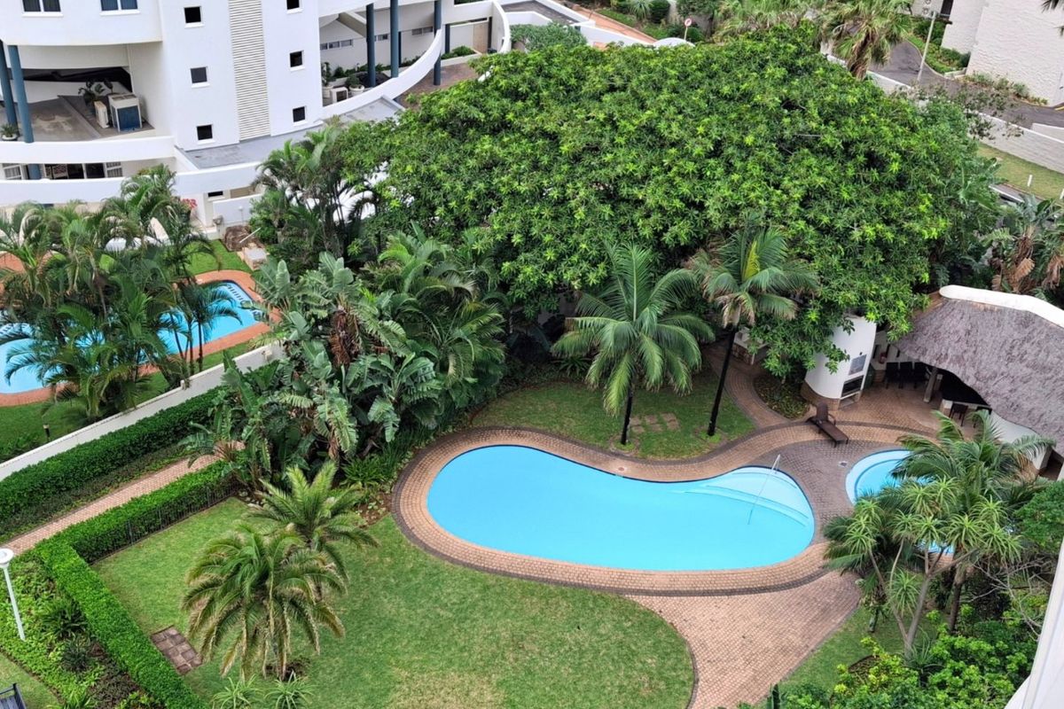 An elevated aerial view of a well-maintained residential complex featuring a swimming pool, thatched entertainment area, and lush landscaped gardens.