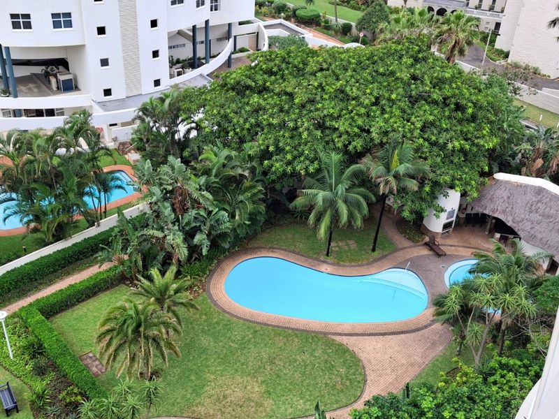 An elevated aerial view of a well-maintained residential complex featuring a swimming pool, thatched entertainment area, and lush landscaped gardens.