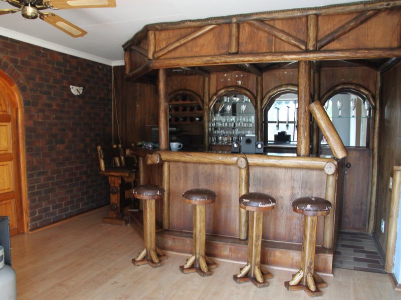 A rustic-style built-in wooden bar area featuring an exposed brick wall, arched shelving, and a ceiling fan.