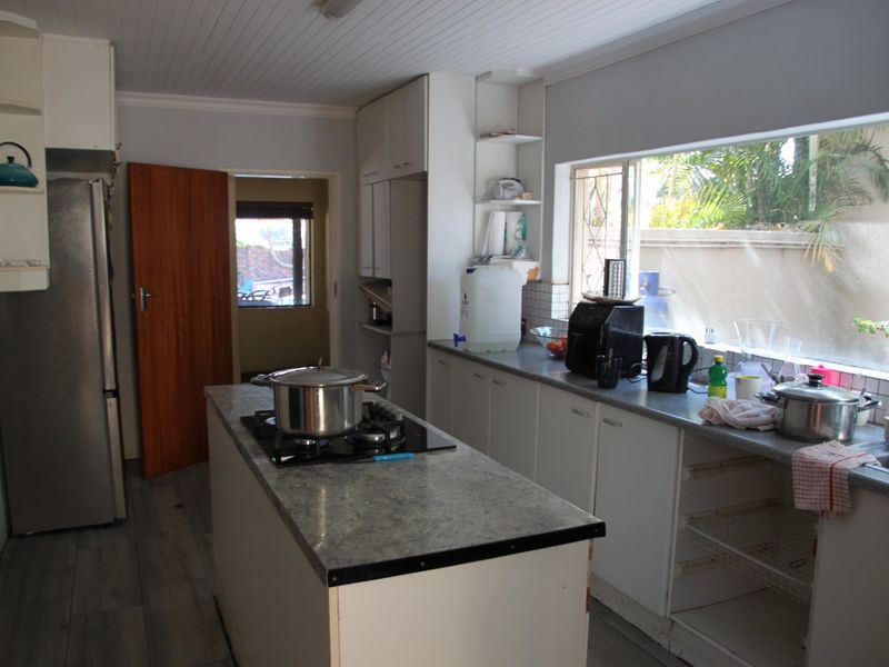 Functional kitchen featuring a central island with a gas hob, ample cabinetry, and laminate flooring, offering a practical layout with potential for cosmetic updates.