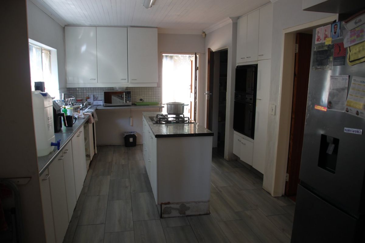 Functional kitchen featuring white cabinetry, a central island with a gas hob, built-in oven, and modern wood-look tiled flooring.