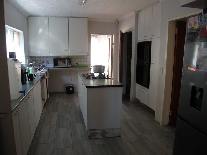 Functional kitchen featuring white cabinetry, a central island with a gas hob, built-in oven, and modern wood-look tiled flooring.