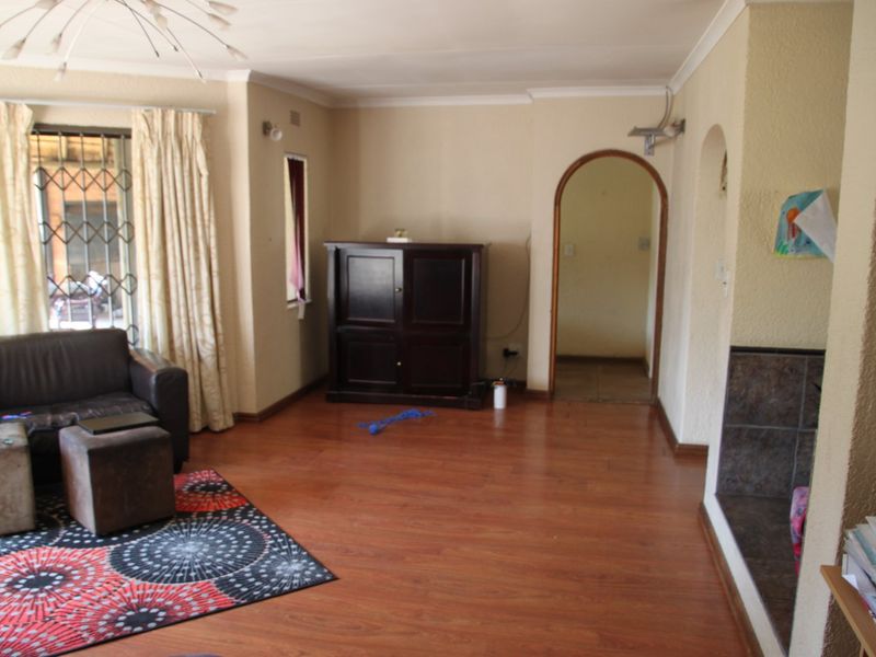 A living room featuring laminate flooring, an arched doorway, and a tiled fireplace hearth, offering a functional space with potential for modernization.