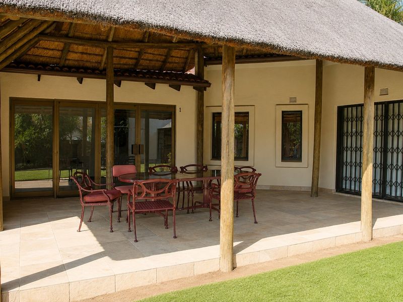 A spacious covered patio featuring a traditional thatched roof, timber support posts, and tiled flooring, providing a seamless transition to the garden area.