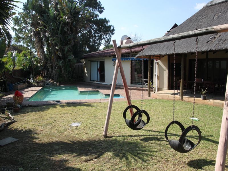 Rear garden view featuring a swimming pool, brick-paved patio area, and a house with a traditional thatched roof.