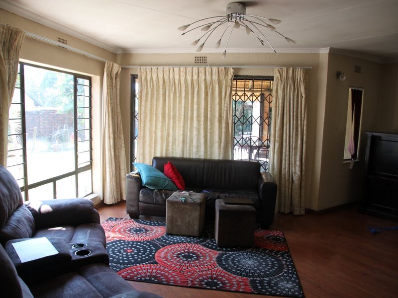 A spacious living room featuring laminate flooring, large windows with security gates, and a central ceiling light fixture, offering a bright and functional living space.