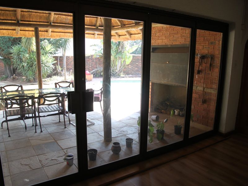 Covered patio area featuring a thatched roof, built-in braai, and stone tile flooring, accessible through large sliding glass doors.