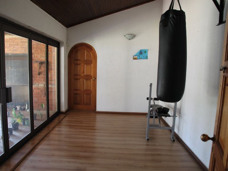 A dedicated gym space featuring laminate flooring, exposed timber ceiling beams, and large sliding glass doors providing access to the outdoor area.