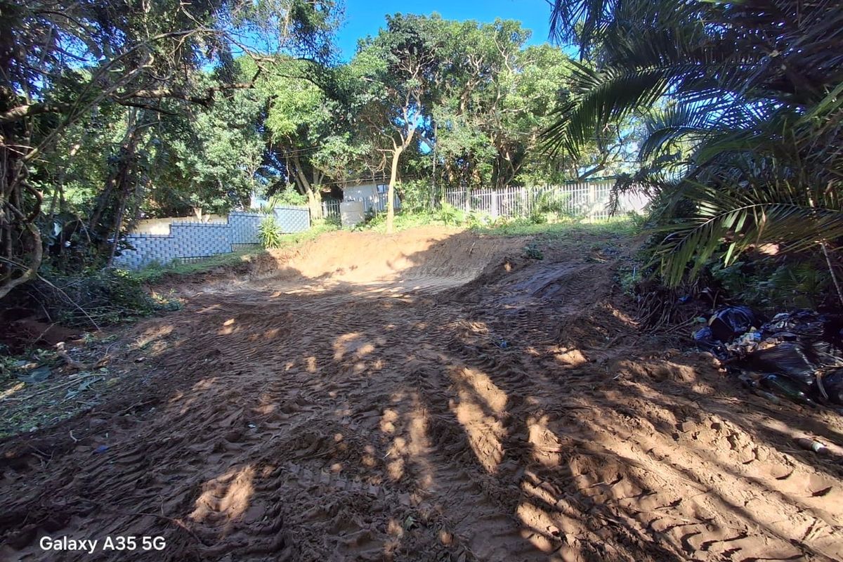 A view of a vacant residential plot featuring cleared earth, mature trees, and perimeter fencing, suitable for future development.