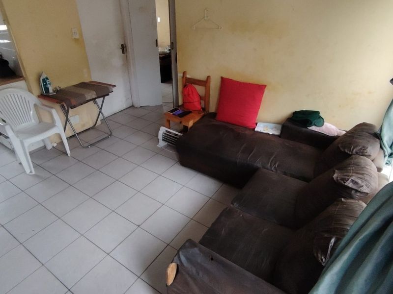 A living room area featuring ceramic floor tiles and multiple internal doors, currently requiring wall repairs and repainting to improve the overall condition.
