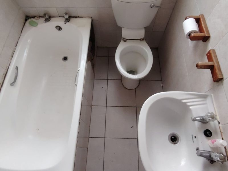 A compact bathroom featuring a standard bathtub, toilet, and washbasin with tiled surfaces, currently requiring maintenance and cosmetic updates.