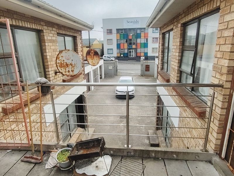 An elevated balcony area with stainless steel balustrades, overlooking a paved courtyard between two brick apartment buildings.