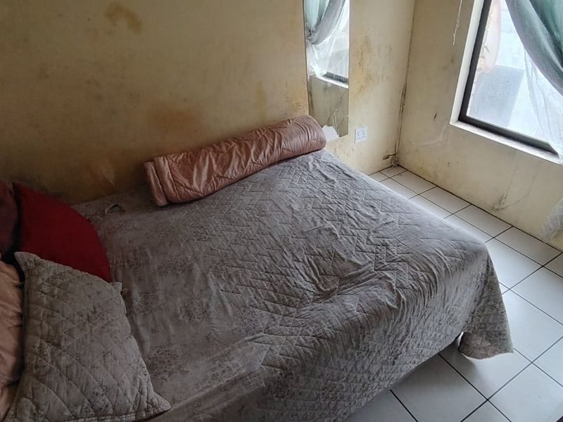 A bedroom featuring tiled flooring and a window, currently showing significant wall staining and surface deterioration requiring maintenance and cosmetic updates.