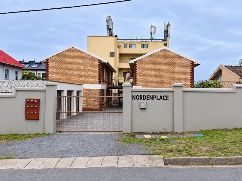 Front view of Nordenplace apartment complex featuring a secure gated entrance, perimeter wall with razor wire, and brick building facade.