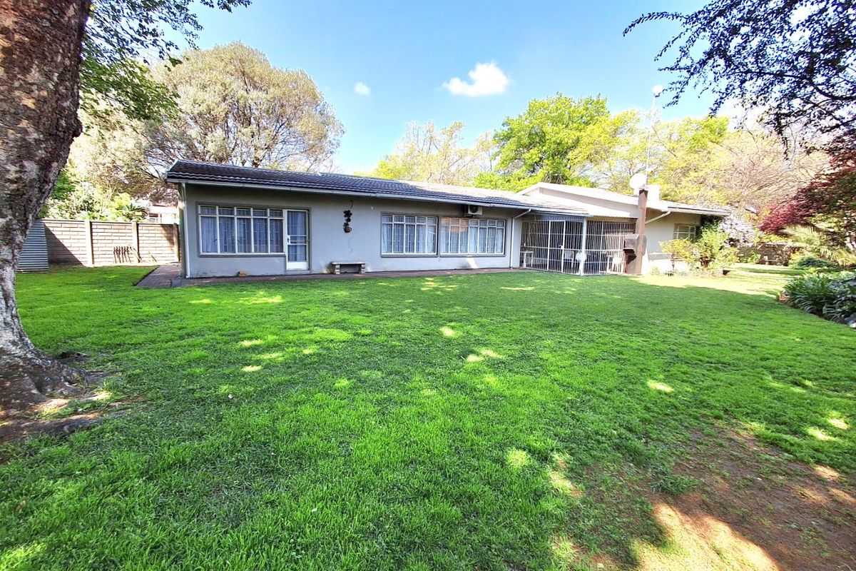 Rear view of the house featuring a spacious lawn, paved patio area, and established garden surroundings.