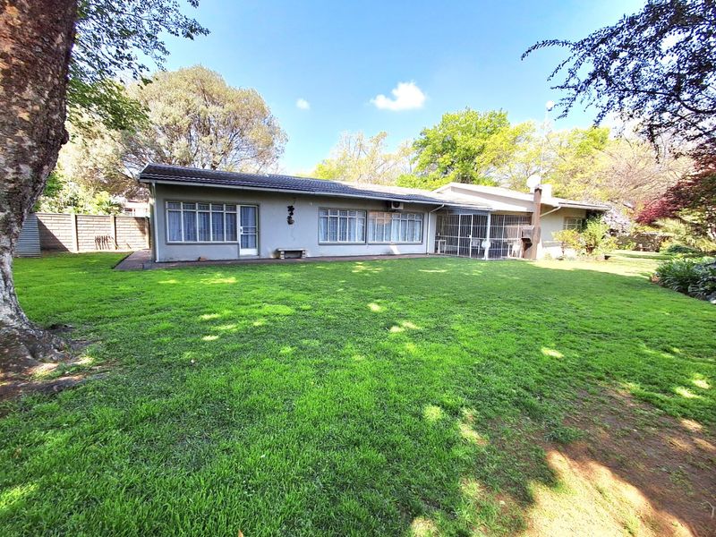 Rear view of the house featuring a spacious lawn, paved patio area, and established garden surroundings.