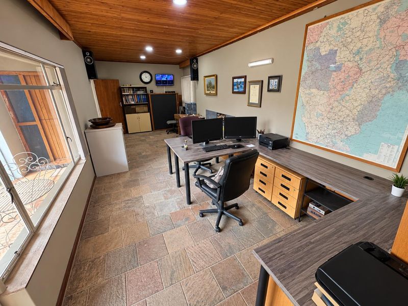 A functional home office featuring stone tile flooring, a warm timber-clad ceiling, recessed lighting, and extensive built-in desk cabinetry.