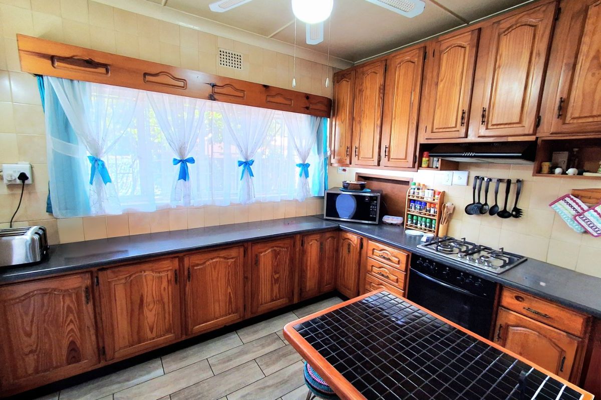 A functional kitchen featuring traditional wooden cabinetry, a gas hob with extractor fan, tiled splashbacks, and a ceiling fan.