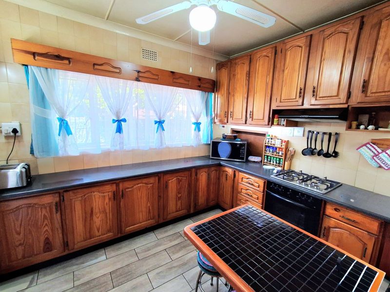 A functional kitchen featuring traditional wooden cabinetry, a gas hob with extractor fan, tiled splashbacks, and a ceiling fan.
