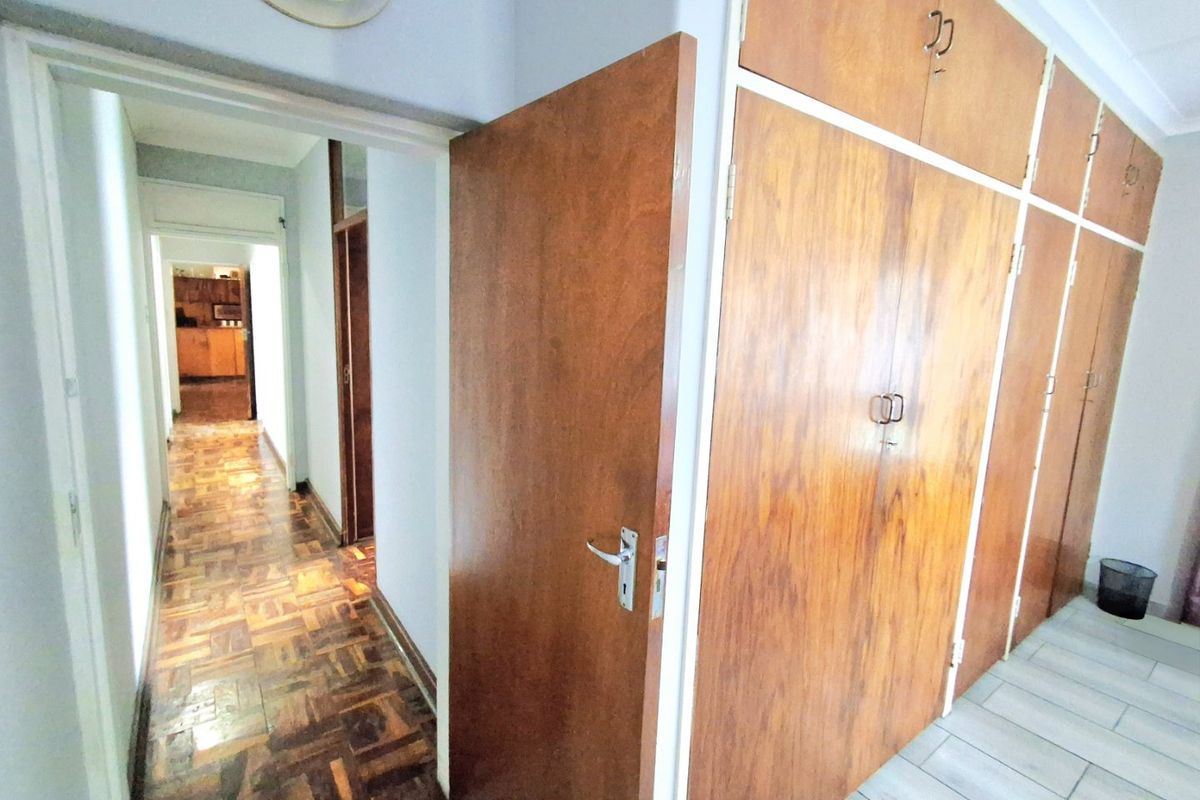 Bedroom featuring extensive built-in wooden cupboards, parquet flooring, and a view through to the hallway and kitchen area.