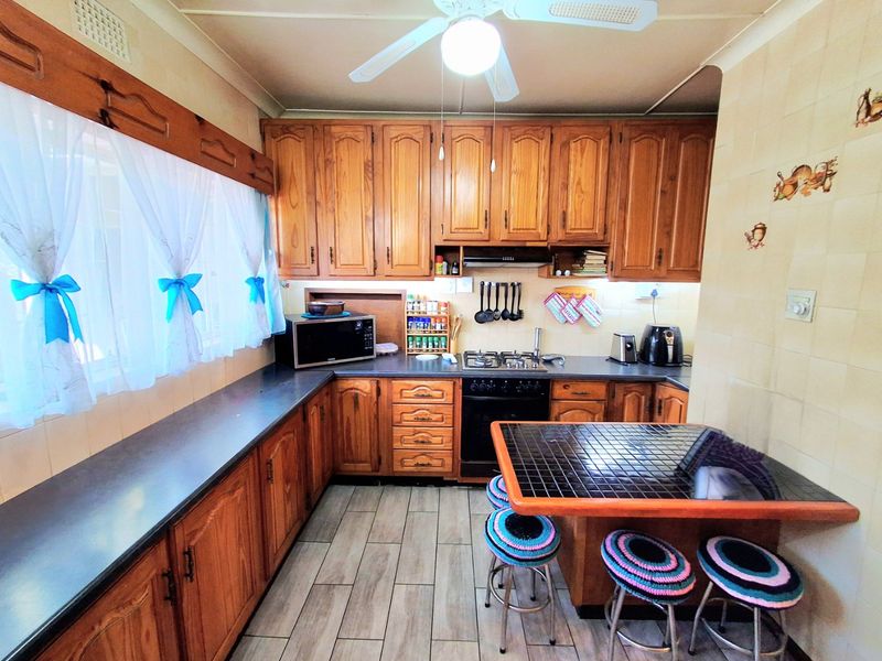A functional kitchen featuring traditional timber cabinetry, gas cooktop, built-in oven, and a tiled breakfast bar area with neutral floor tiling.