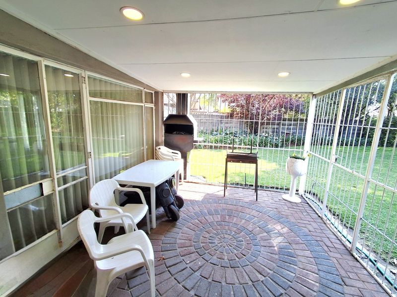 Covered patio area featuring brick paving, a built-in braai, and secure metal screening, providing direct access to the garden.