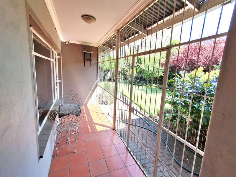 A covered patio area featuring tiled flooring and secure metal security bars, providing direct access to the garden.
