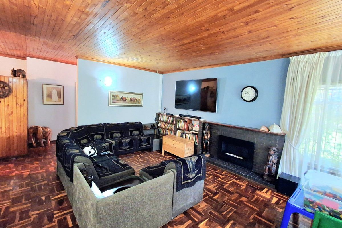 Spacious living room featuring warm timber tongue and groove ceilings, classic parquet flooring, and a central brick fireplace with integrated shelving.