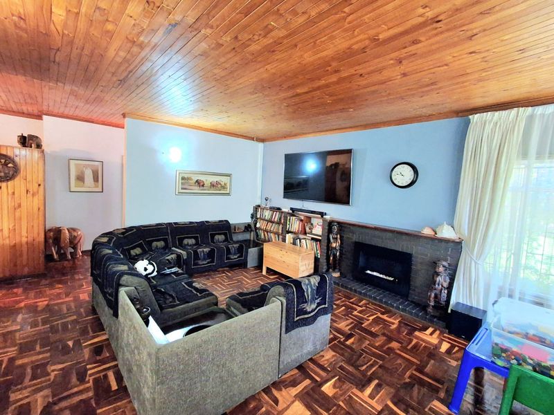 Spacious living room featuring warm timber tongue and groove ceilings, classic parquet flooring, and a central brick fireplace with integrated shelving.