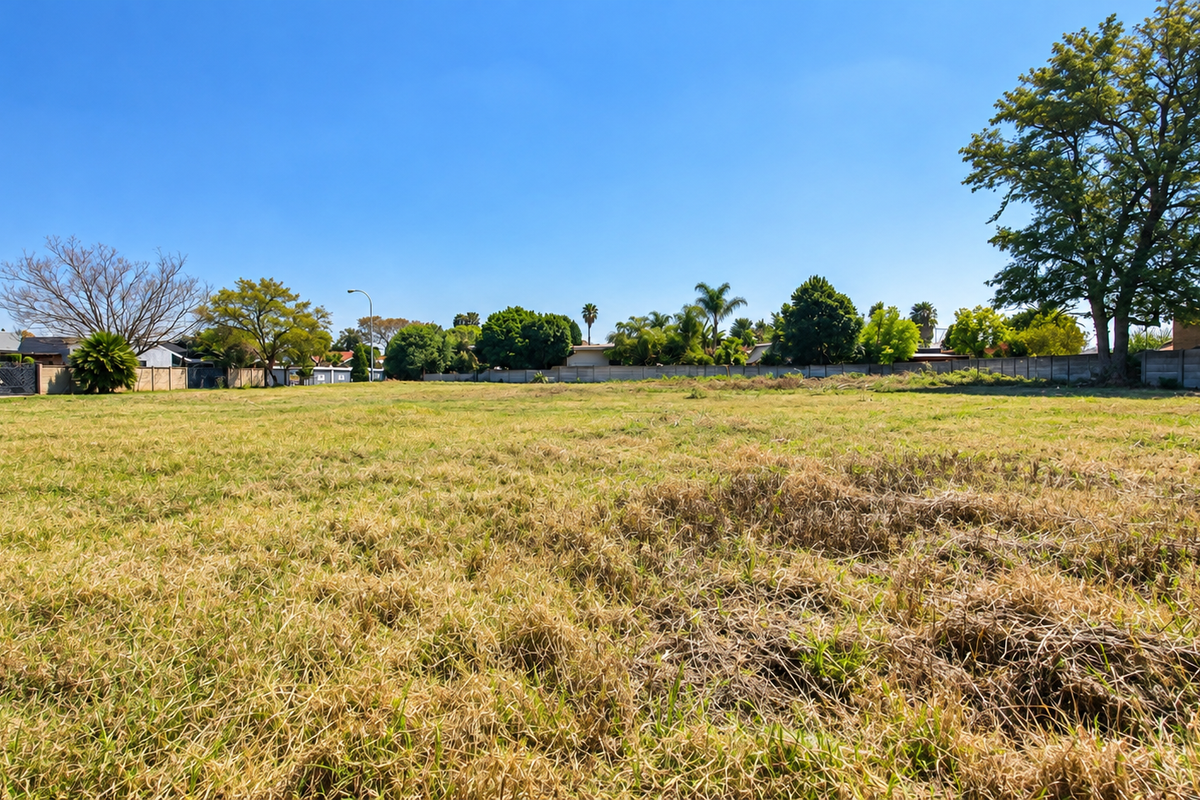 A spacious, level vacant residential plot featuring established perimeter walls and mature trees, offering a blank canvas for future development.