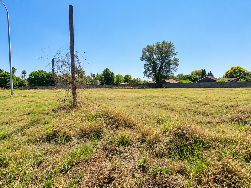 A vacant residential plot of land featuring a concrete perimeter wall and street-side access, ready for development.