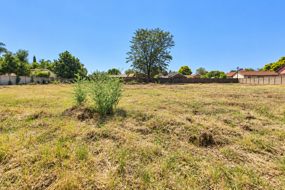 A vacant residential plot of land featuring a perimeter wall and established trees, offering a clear space ready for development.