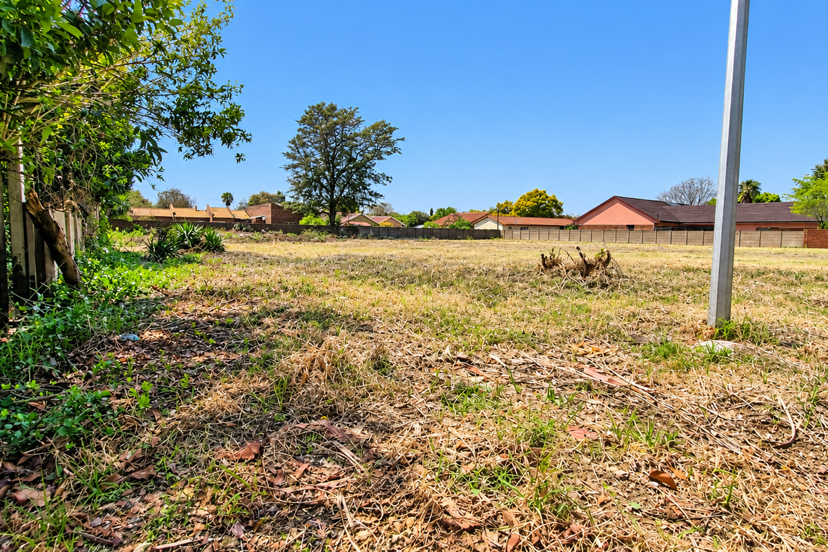 A vacant residential plot featuring dry grass, established perimeter fencing, and a metal utility post, offering a clear space for future development.