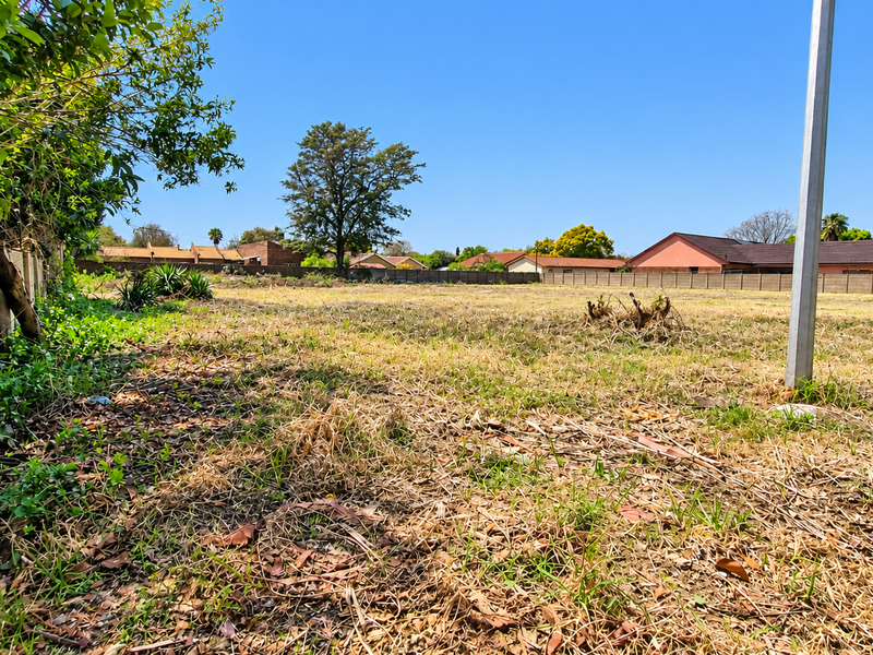 A vacant residential plot featuring dry grass, established perimeter fencing, and a metal utility post, offering a clear space for future development.