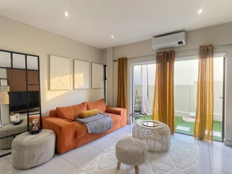 A bright and modern living room featuring tiled flooring, recessed lighting, a wall-mounted air conditioning unit, and large sliding glass doors leading to a patio.