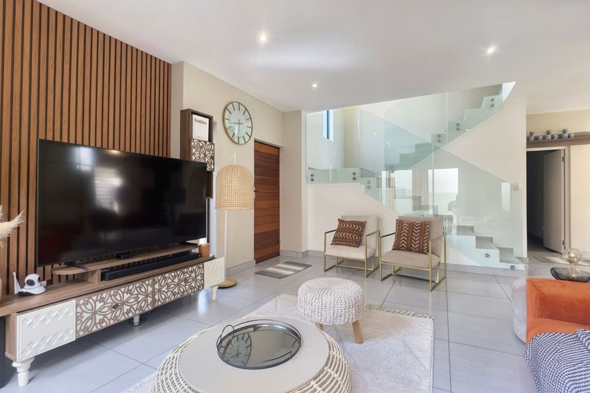 Modern open-plan living area featuring a stylish slatted timber accent wall and a contemporary staircase with glass balustrades and tiled flooring.