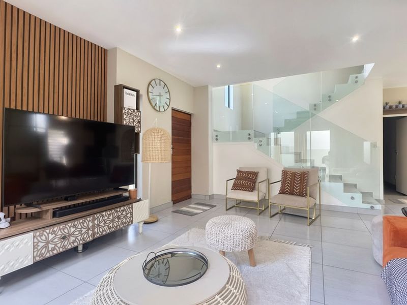 Modern open-plan living area featuring a stylish slatted timber accent wall and a contemporary staircase with glass balustrades and tiled flooring.