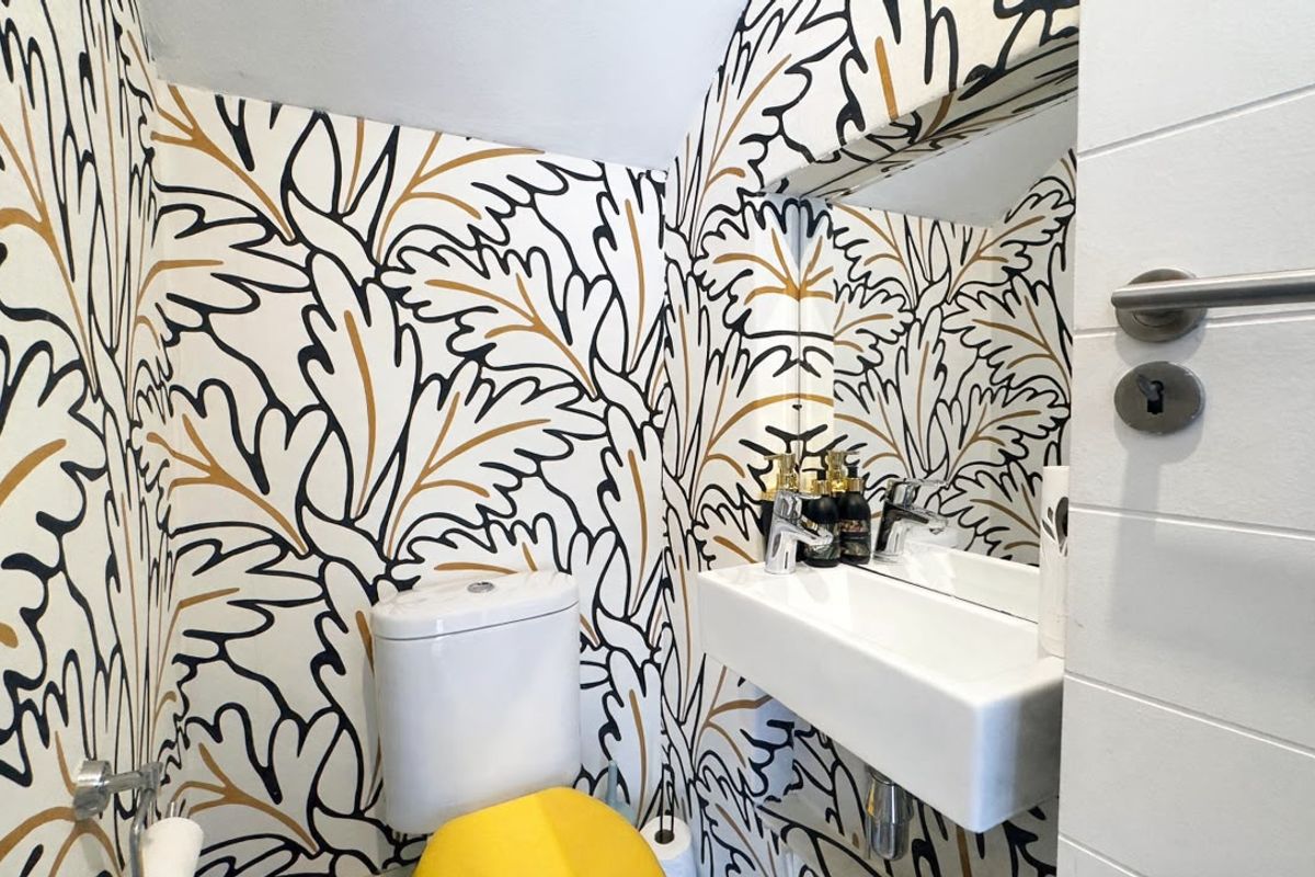 A compact powder room featuring a wall-mounted basin, chrome fixtures, and bold patterned wallpaper.