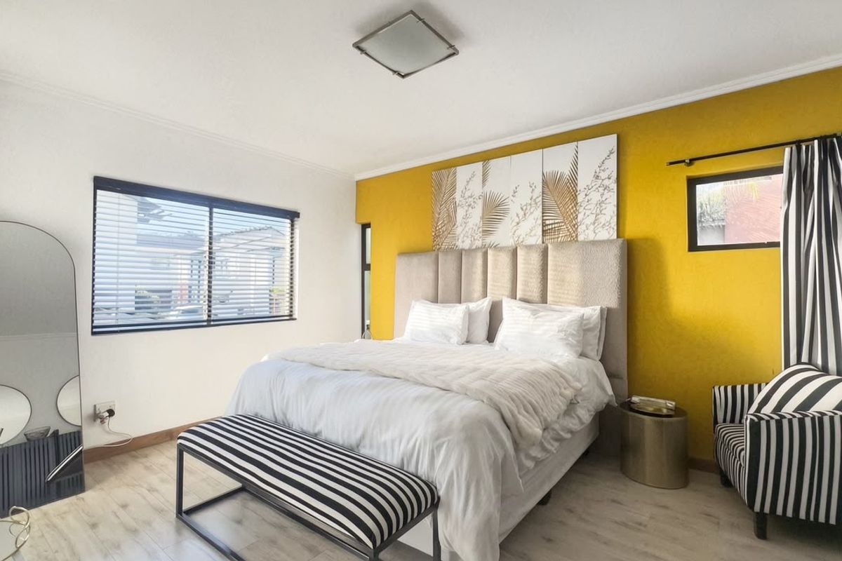 A well-maintained bedroom featuring laminate flooring, neutral wall finishes with a vibrant accent wall, and natural light provided by a window with venetian blinds.