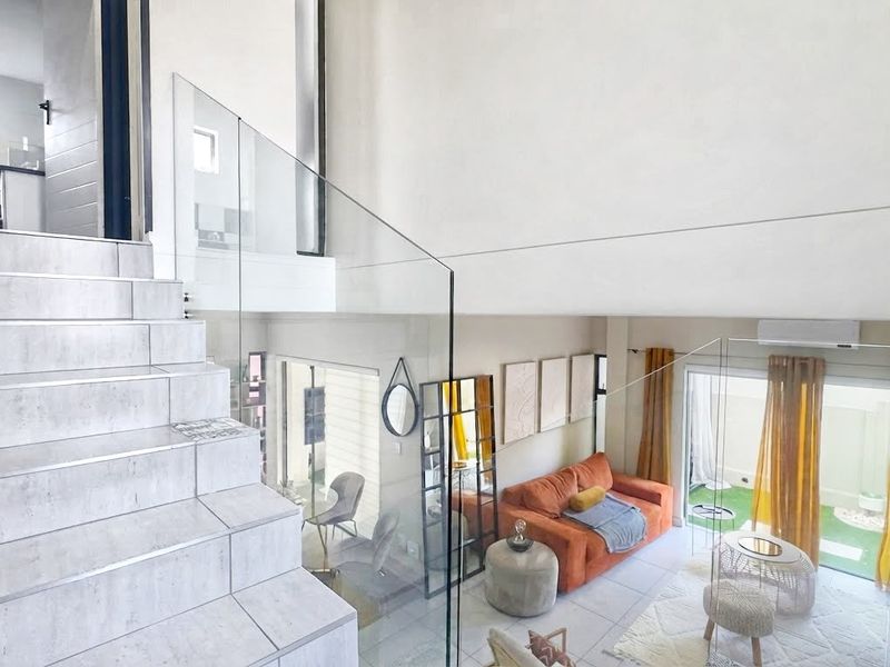 Modern open-plan living area featuring a tiled staircase with a sleek glass balustrade, leading to a bright, airy space with direct access to the outdoors.