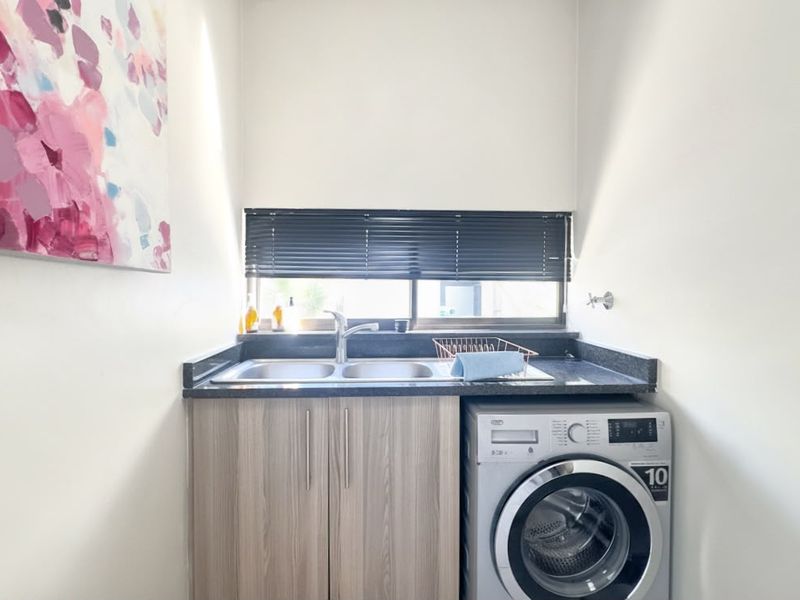A functional laundry area featuring a stainless steel double sink, stone countertop, and built-in cabinetry with space for a washing machine.