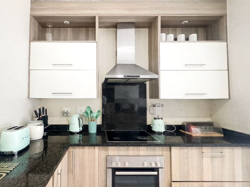 Modern kitchen featuring light wood-grain cabinetry, contrasting black granite countertops, a built-in oven, and a stainless steel extractor fan.